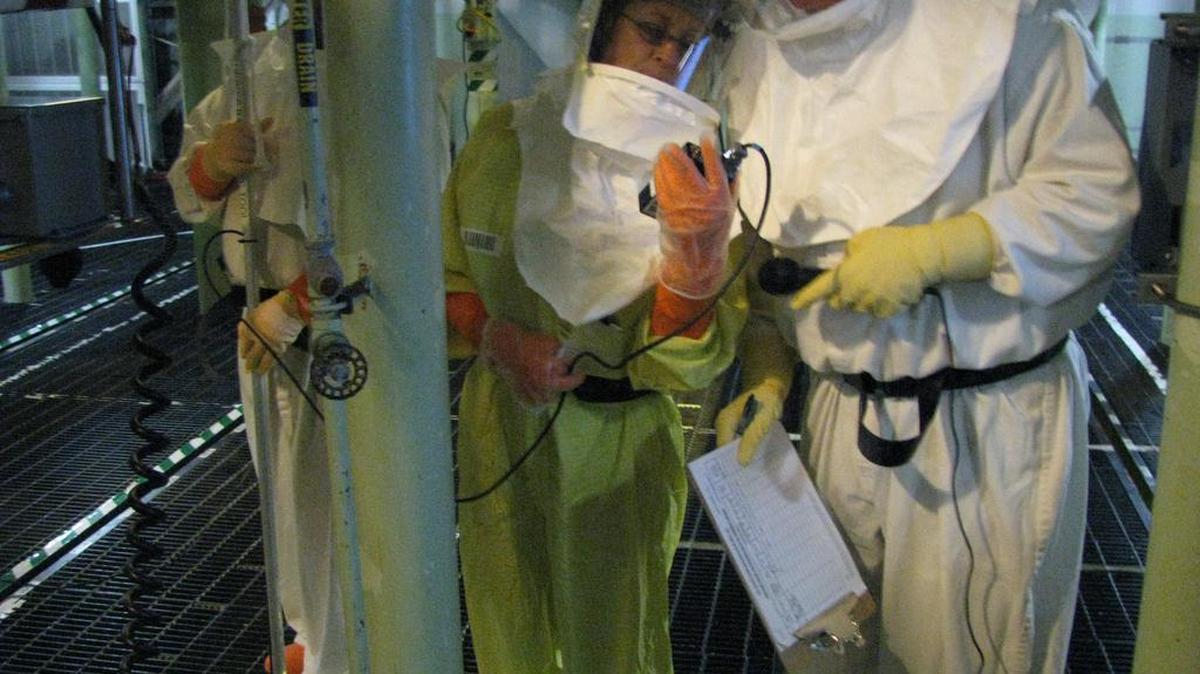 Employees inside the 100 K West reactor fuel storage basin wear protective equipment as they prepare the basin for the installation of sludge retrieval equipment.