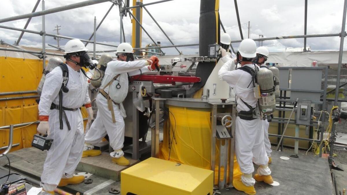 WRPS used an innovative suite of tools to remove a highly contaminated pump from double-shell tank AW-106. This photo shows a field worker, second from left, operating a mechanical lever to close foam insulation that wraps around the pump column. Meanwhile, health physics technicians take readings prior to the operators installing the zip ties around the foam.
