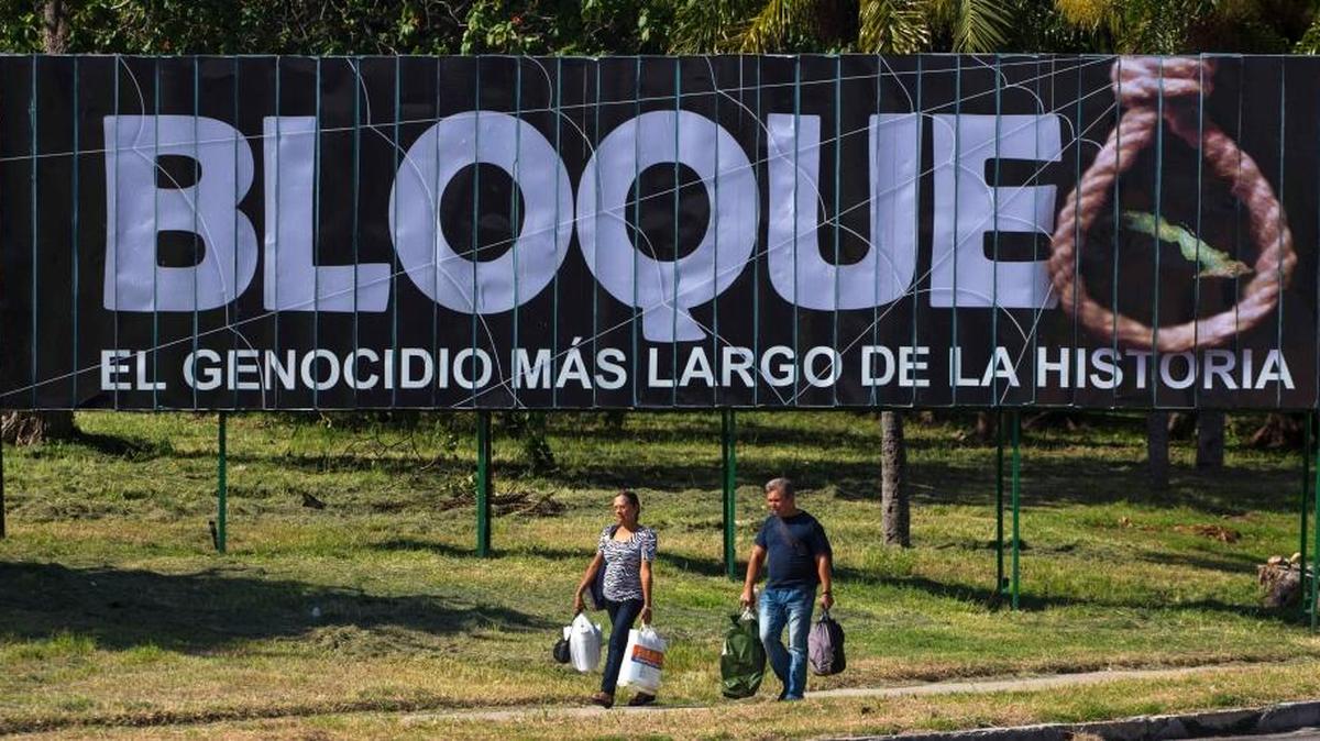 People walk to the bus terminal in October 2015, past a billboard that reads in Spanish: “Blockade, the longest genocide in history” in Havana, Cuba.