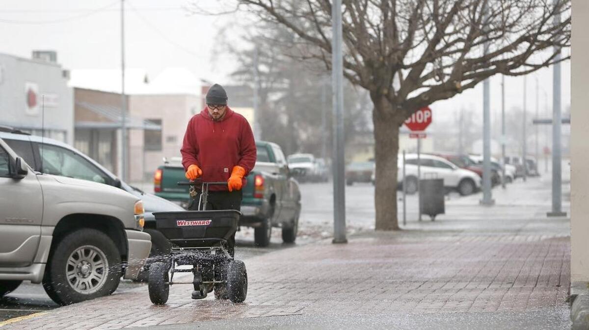 A Franklin County Facilities employee spreads granular ice melt on an ice encrusted sidewalk in Pasco.