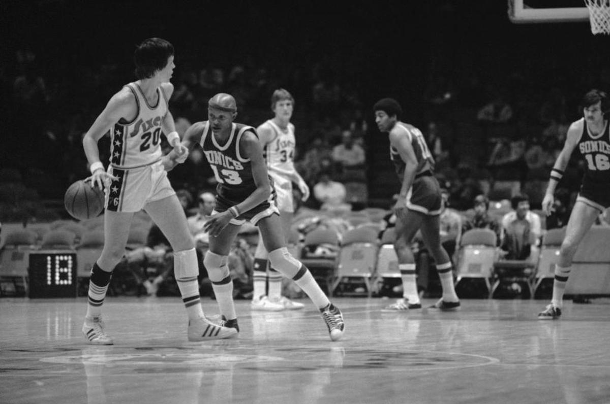 Seattle’s Slick Watts (13) reaches around Philadelphia’s Doug Collins (20) to tip the ball away for a steal in this 1975 game in Philadelphia.