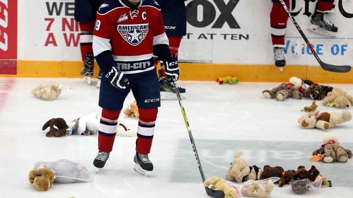 Tri-City Americans’ Tyler Sandhu (19) smiles as he uses his stick to move a teddy bear after scoring the first goal Saturday during the team’s annual Teddy Bear Toss game against the Victoria Royals at Toyota Center in Kennewick. Sandhu scored 36 seconds into the game, setting a team record for the fastest Teddy Bear goal. See more photos at www.tricityherald.com.